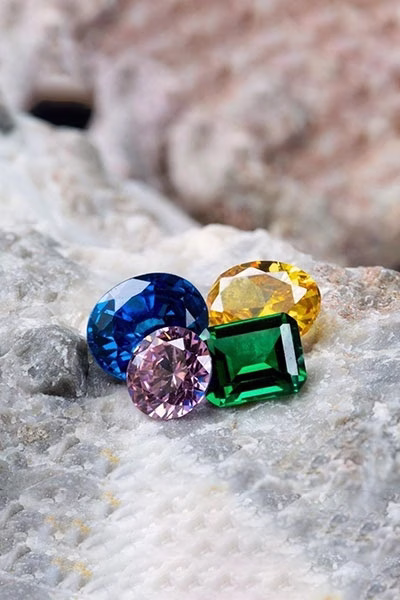Four vibrant gemstones in blue, pink, green, and yellow showcased by DBT Diamonds (Diamond Board of Trade)