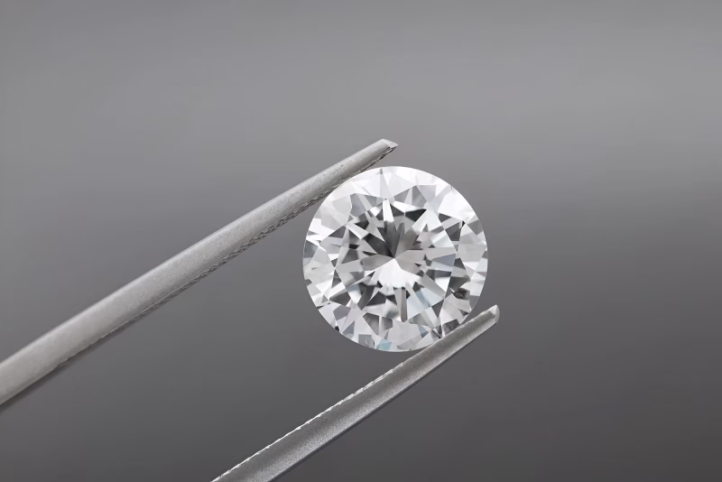 A round brilliant-cut diamond held by precision tweezers against a neutral gray background.